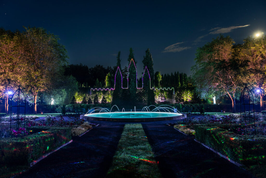 Overview of a nighttime garden experience featuring laser projections creating a castle design across the landscape.