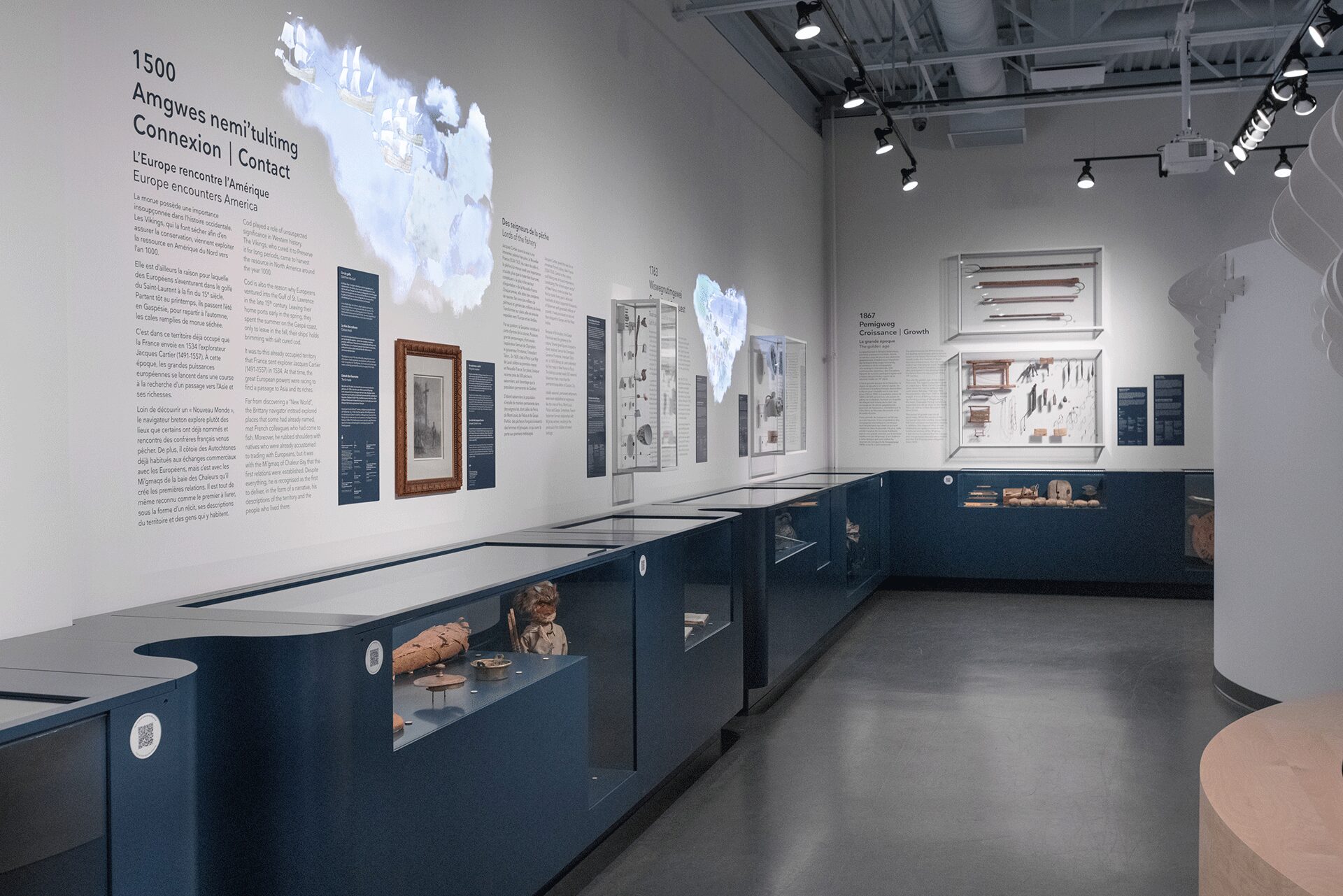 Museum walkway at the Musée de la Gaspésie featuring display cases with artifacts and animated wall projections, creating an immersive experience.
